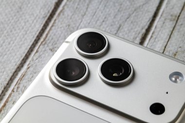 Yılan pençesi. Polonya. 7 Kasım 2025. Ahşap arka planda, zarif metalik tasarım ve gelişmiş akıllı telefon teknolojisini gösteren iPhone 17 Pro kamera lenslerinin makro görüntüsü.