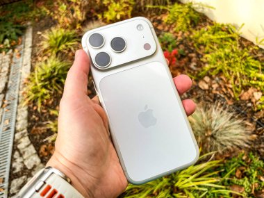 Yılan pençesi. Polonya. 14 Kasım 2025. Bir el, MagSafe bataryasıyla gümüş bir iPhone 17 profesyonelini tutuyor. Açık havada çekilmiş, arka planda bulanıklık var..