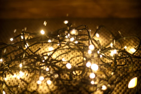 Örgü bir arka planda parlayan peri ışıklarının yakın çekimi. Sıcak ve rahat bir festival sahnesi, Noel dekoru, kış atmosferi ya da Noel temalı içerik için mükemmel..