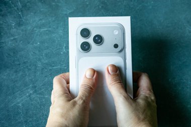 Yılan pençesi. Polonya. 7 Kasım 2025 Hands beyaz bir iPhone 17 profesyonel kutusunu koyu dokulu arka planda tutuyor. Modern akıllı telefon ambalajının yakın çekimi. Teknik boks kavramı.