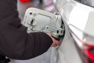 Yakıt kapağı menteşesi ve araç gövdesinin mekanik detaylarını gösteren beyaz bir arabanın yakıt deposunun kapağını açan kişinin elini kapatın..