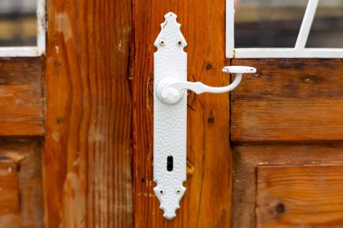 Kırsal ahşap kapı kolunda eski beyaz metal kapı kulpu desenli detaylar ve yumuşak bulanık arka plan.