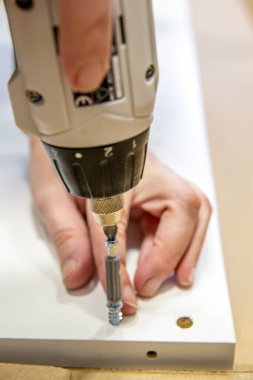 Montaj sırasında donanımı bir mobilya tahtasına vidalamak için kablosuz matkap kullanan bir kişinin yakın plan görüntüsü.