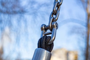 Metal zincire yakın çekim ve ipe bağlanma. Endüstriyel bağlantı ayrıntıları açık havada güç, güvenlik ve dayanıklılığı vurguluyor.