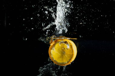 Taze portakal dilimi suya güçlü bir sıçrama ve siyah arka planda kabarcıklar ile vurur. Tazelik, enerji, hareket, sağlıklı beslenme ve vitamin açısından zengin gıdalar..