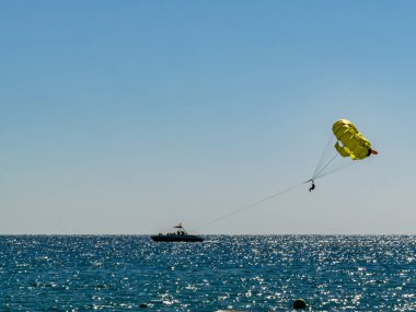 Sarı bir paraşüt ve ufukta bir tekne ile denizin üzerinde paraşütle iniyordu. Yaz tatili, su sporları, özgürlük ve macera konsepti, açık gökyüzü ve parlak okyanus.