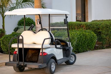 Elektrikli golf arabası otel binasının yakınındaki lüks bir tatil yerine park edilmiş. Misafirler için çevre dostu ulaşım, konukseverlik hizmeti, tatil seyahati ve turizm kavramı.