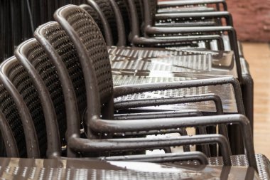 Yağmurdan sonra ıslak metal sandalyeler. Su damlacıkları ve tekrar eden perspektif çizgileri olan kentsel kafe mobilyaları.