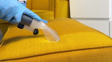 Mavi koruyucu eldiven giyen birinin sarı döşeme yastığını vakum hortumuyla temizlerken videosu. Kapalı bir ev ortamında kumaşın derin temizlik sürecinin yakın plan görüntüsü.