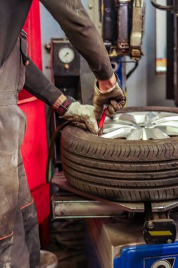 Koruyucu eldivenli tamirci otomotiv atölyesinde lastik değiştirme makinesinin lastiklerini tamir ediyor. Profesyonel araç bakım ve lastik servisi..