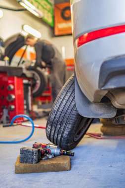 Otomobil tamirhanesinde araç tamiri sırasında arka planda tamirci çalışırken araç tekerleklerini ve araçları kapat.