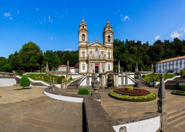 Bom Jesus, Braga 'da barok kilise cephesi, zigzag merdivenleri ve parlak resmi bahçeleriyle aydınlık bir yaz gökyüzü altında UNESCO manzarası altında tek bir sığınak yapıyor.
