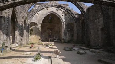 Cambados, Galiçya, İspanya 'daki tarihi bir kilisenin antik taş kemerlerini ve kalıntılarını gösteren sinematik yukarı doğru eğik bir video. Güneşli bir tatil beldesinde mimarlık, miras ve kültür turizmi.