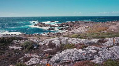 İspanya 'nın Galiçya kentindeki engebeli Atlantik kıyısının çarpıcı panoramik manzarası. Turkuaz okyanus dalgaları güneşli bir yaz tatilinde açık mavi gökyüzü altında kayalıklara çarpıyor.