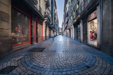Casco Viejo, Bilbaos 'un eski bir kasabası, sabahın erken saatlerinde geleneksel binalar ve kapalı dükkanlarla dolu boş bir kaldırım taşı caddesini sergiliyor. Bilbao İspanya 20 Ekim 2025