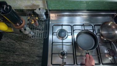 Çelik bir gaz sobasının üzerine tava koyan bir insanın yavaş çekim görüntüsü ve sonra uzun bir mutfak çakmağı ile ocağı yakmak, evde yemek pişirmeye hazırlanmak.