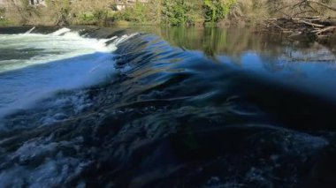 Güneşli bir günde, sakin bir şekilde akan bir nehrin berrak suları Galiçya 'daki Camino de Santiago hac yolunda beyaz köpük ve hafif dalgalar oluşturur.