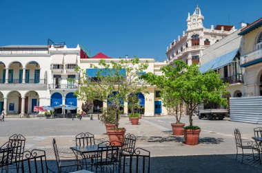Eski Havana, Küba 'daki Plaza Vieja, güneşli bir günde tarihi sömürge mimarisini sergiliyor, açık hava kafeleri ve ağaçlarıyla birlikte, kültürel ve seyahat kavramları sunuyor.