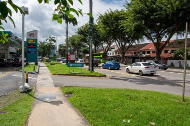 Bir benzin istasyonu, yoldaki araçlar ve yemyeşil yemyeşil yoğun bir kavşak. Sahne mavi bir taksi ve beyaz bir sedan da dahil olmak üzere sokakları saran dükkanlar ve ağaçlarla dolu bir araba karışımını yakalıyor..