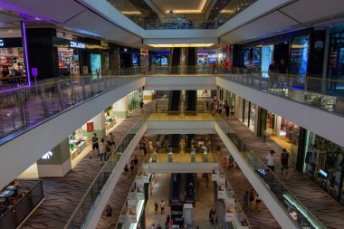 Çok katlı modern bir alışveriş merkezi. Yürüyen merdivenler ve çeşitli dükkanlar var. Müşterilerle dolup taşıyor.