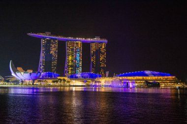 Suya yansıyan aydınlık binalarla modern bir mimari mucizenin çarpıcı gece görüntüsü.