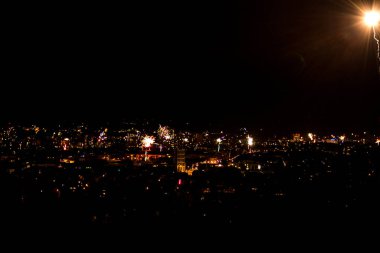 Havai fişeklerle aydınlatılan bir gece şehri. Karanlık gökyüzüne karşı çeşitli renklerde canlı bir gökyüzü sergiliyor.