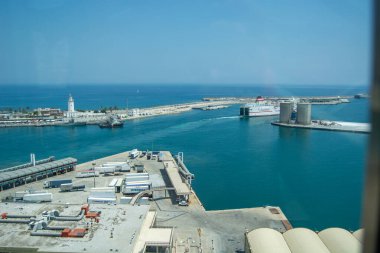 Temiz bir gökyüzünün altında gemi, vinç ve mavi suya sahip bir limanın havadan görüntüsü.