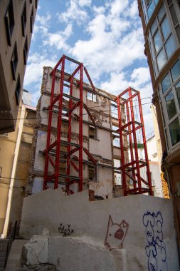 Modern binalarla çevrili, bulutlu bir gökyüzünün altında kısmen yıkılmış kırmızı çelik iskeleti olan bir bina.