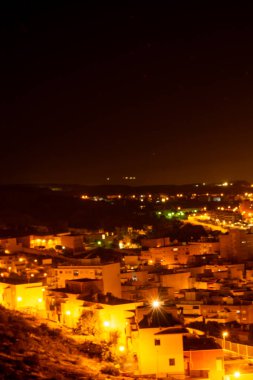 Aydınlatılmış binalar ve caddelerle dolu bir gece şehri, canlı bir şehir atmosferi sergiliyor.