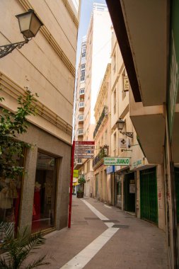 Binalar arasındaki dar sokaklar, üzerinde açık mavi gökyüzü olan dükkanlar ve tabelalar