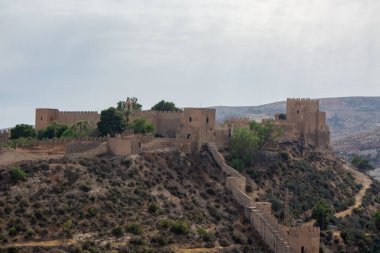 A historic castle on a hill surrounded by rocky terrain and sparse vegetation