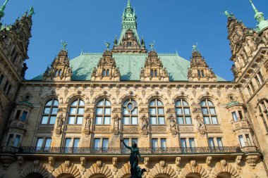 Süslü mimarisi olan tarihi bir bina, açık mavi gökyüzünün altında yeşil bakır bir çatı ve heykeller var.