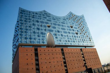 Benzersiz bir cam cepheli ve tuğla tabanlı, açık mavi gökyüzüne karşı kurulmuş modern bir mimari bina.