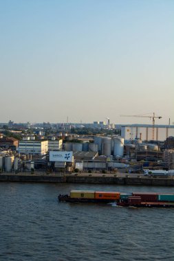 Nehir kenarında depolama tankları, binalar ve kargo gemisinin bulunduğu sanayi bölgesinin manzarası.