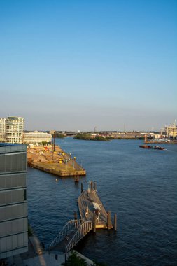 Rıhtımı olan bir nehir manzarası, sahildeki binalar ve açık mavi bir gökyüzü.