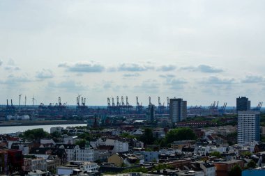Gökyüzünün altında vinçler ve rüzgar türbinleri olan bir şehrin panoramik görüntüsü