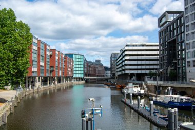Her iki tarafında binalar bulunan, berrak mavi bir gökyüzü ve su yolu boyunca kenetlenmiş teknelerin yer aldığı modern şehir kanalının manzarası.