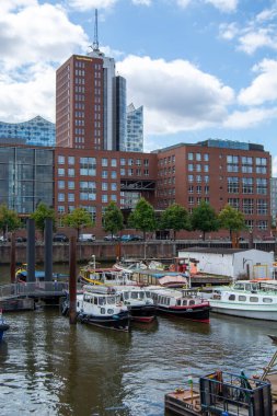 Modern binalar ve berrak mavi gökyüzü ile çevrili çeşitli teknelerle dolu bir liman manzarası.