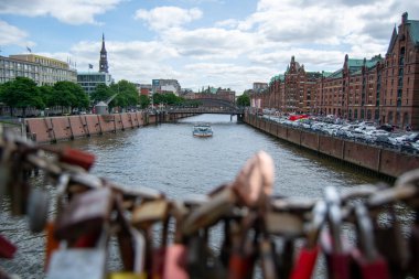 Parçalı bulutlu bir gökyüzünün altında tarihi binalar ve ağaçlarla çevrili, teknesi olan bir nehrin manzarası.