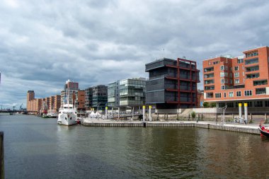 Nehir boyunca çağdaş binaların olduğu, teknelerin kenetlendiği ve gökyüzünün bulutlu olduğu modern bir rıhtım manzarası.