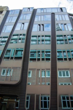 Geniş cam pencereler ve dalgalı çizgiler, cam ve tuğladan oluşan zıt materyaller içeren eşsiz bir cepheli modern mimari yapı.