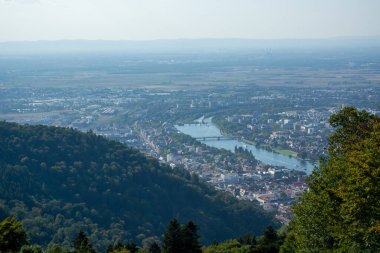 Tepeler ve yeşilliklerle çevrili bir şehirde kıvrılan bir nehrin havadan görünüşü.