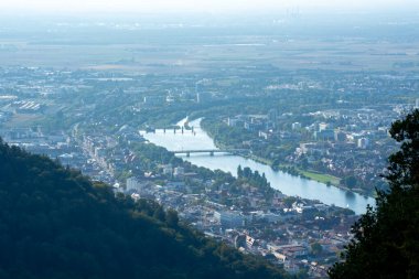 Etrafı yeşillik ve tepelerle çevrili bir şehirde kıvrılan bir nehrin havadan görünüşü.