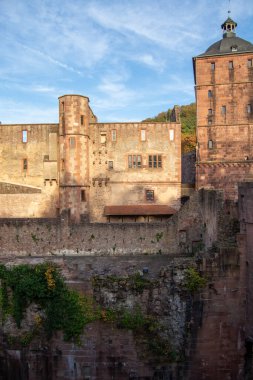 Taş duvarları, kuleleri ve bulutlu mavi gökyüzünün altında kayalık bir uçurumu olan tarihi bir şato.