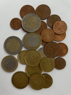 Beyaz bir yüzeye saçılmış karışık avro sikkeleri koleksiyonu. Görüntü bakır gümüş ve altın tonlarını da içeren çeşitli metalik renkleri gösteriyor. Kompozisyon vurgulanıyor