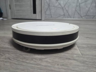 Modern apartman içinde ahşap kaplama zeminde çalışan beyaz robotik elektrikli süpürge. Otomatik zemin temizleme ve günlük bakım için tasarlanmış akıllı ev aletleri. Olağanüstü.