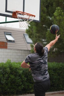 Bir adam basket topunu dış çembere doğru atıyor, spor ve egzersiz yapıyor.