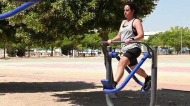 Spor giyim sektöründe kararlı bir kadın açık hava spor salonunda eliptik bir çapraz antrenör kullanıyor.