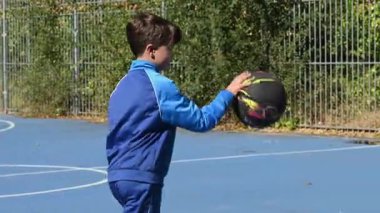 Mavi eşofman giyen atletik çocuk dışarıda basketbol oynuyor.