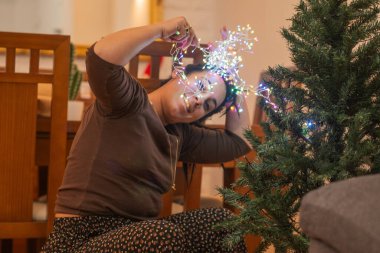 Noel ağacını renkli ışıklarla dekore eden bir kadın.